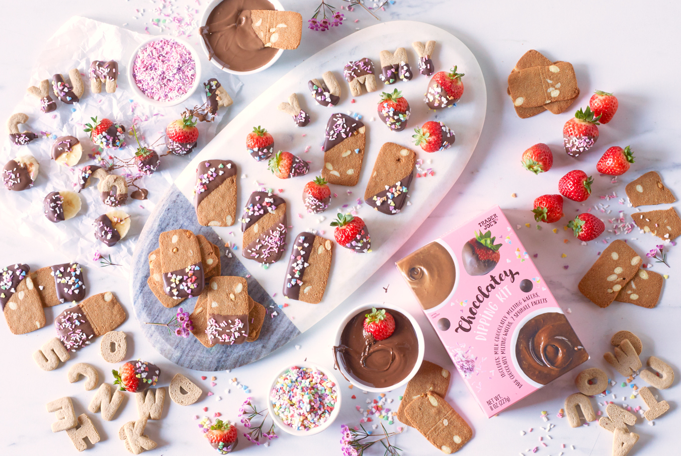 BTrader Joe's Chocolatey Dipping Kit; small dishes with milk and dark melted chocolate, small dishes with sprinkles, platter with strawberries and two kinds of cookies, dipped with chocolate and sprinkles
