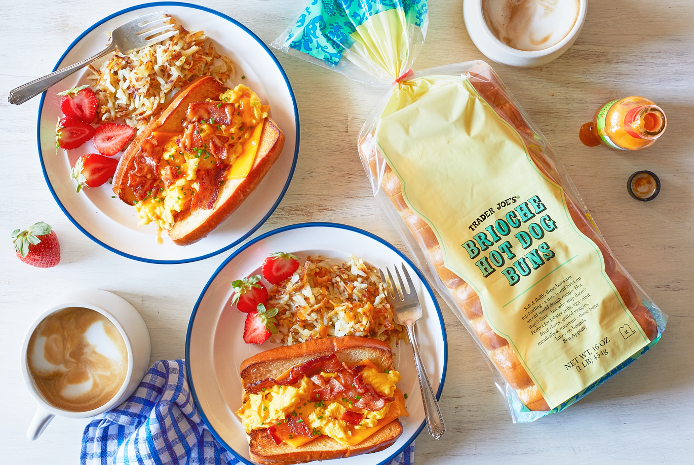 Trader Joe's Brioche Hot Dog Buns; shown as a 'Breakfast Bun', with scrambled eggs, bacon, cheese in a toasted brioche hot dog bun. On two plates with hashbrowns and sliced strawberries