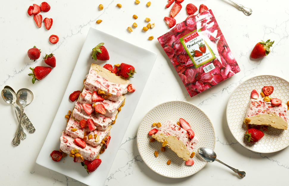 PB&J Semifreddo loaf, sliced on a serving platter next to individual slices on plates, surrounded by fresh strawberries and a bag of Trader Joe's Freeze Dried Strawberries