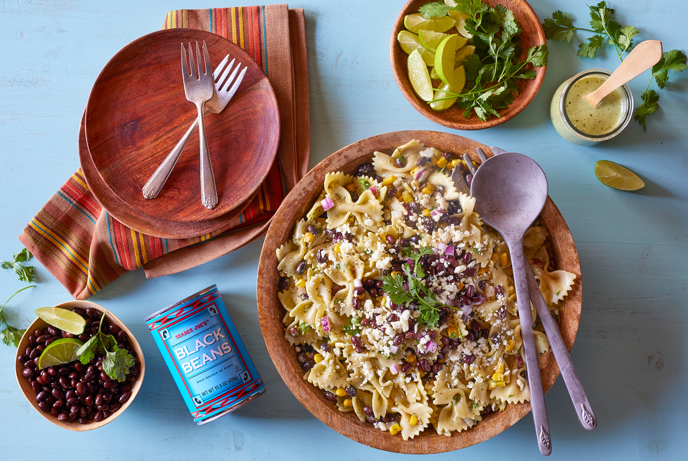 Trader Joe's Roasted Corn used in recipe for Chicken Fajita Bowl; wood surface with 2 black bowls containing sliced grilled chicken, black beans, roasted corn, sliced peppers and onions, and sliced avocado - on top of rice; with lime and cilantro garnish