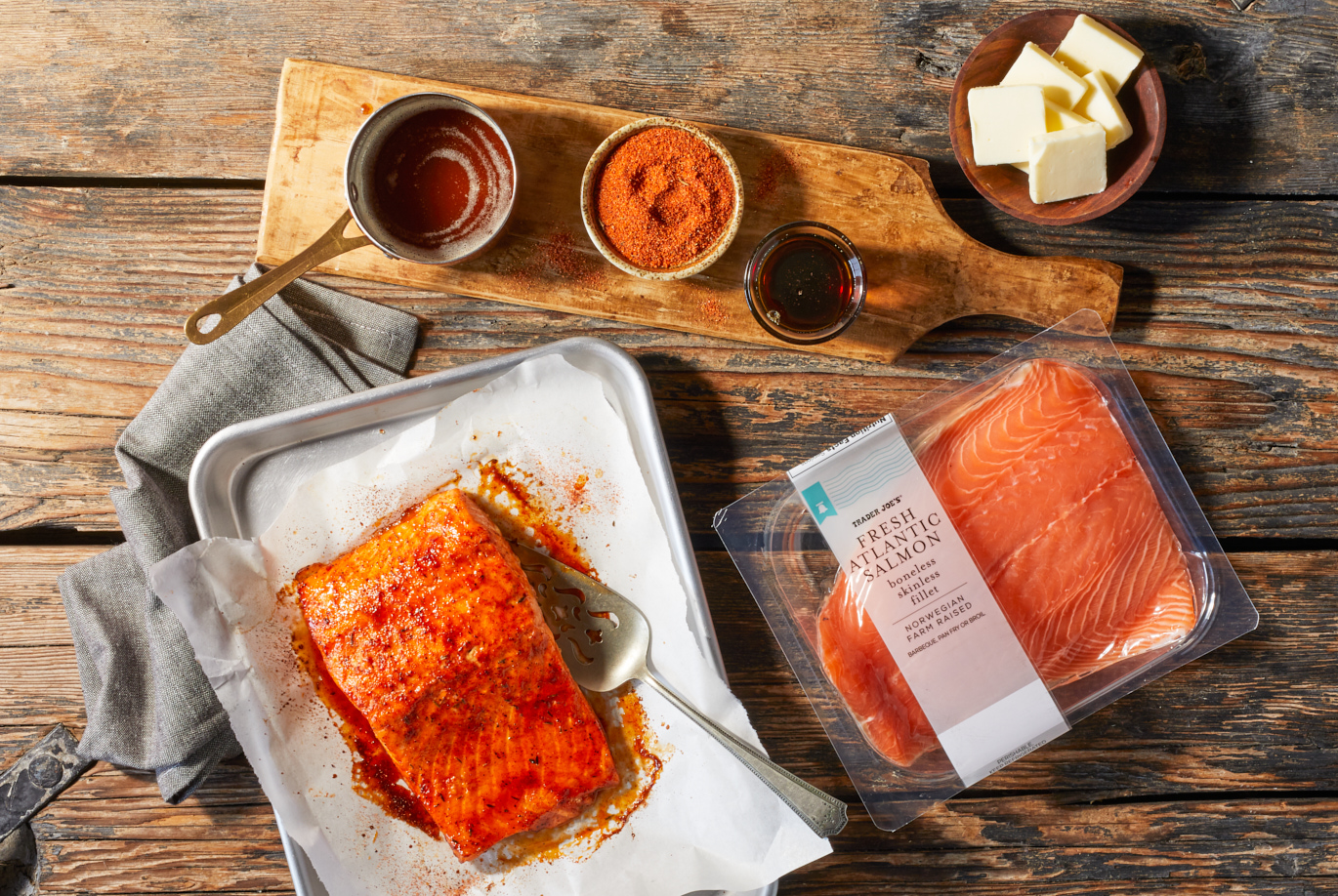 Trader Joe's Fresh Atlantic Salmon; shown in recipe for Maple & Brown Butter Salmon; a rustic wood surface with roasted salmon on baking sheet; prep ingredients above showing butter, brown butter, salmon rub and maple syrup