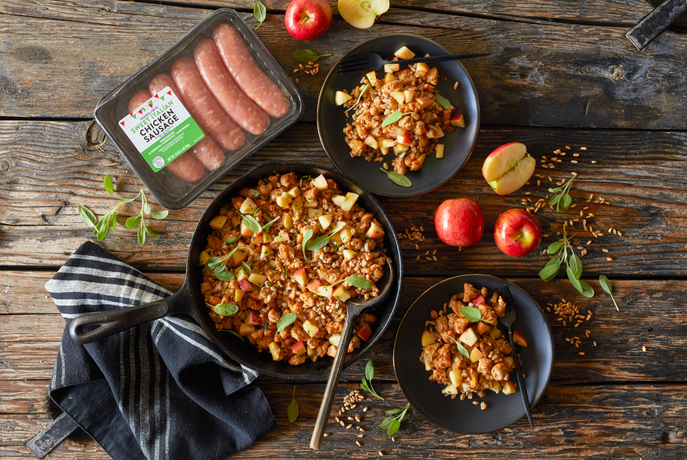 Trader Joe's Sweet Italian Chicken Sausage used in recipe for Farro with Chicken Sausage; served in a cast iron skillet and two plates, dried farro, apples and sage leaves on surface